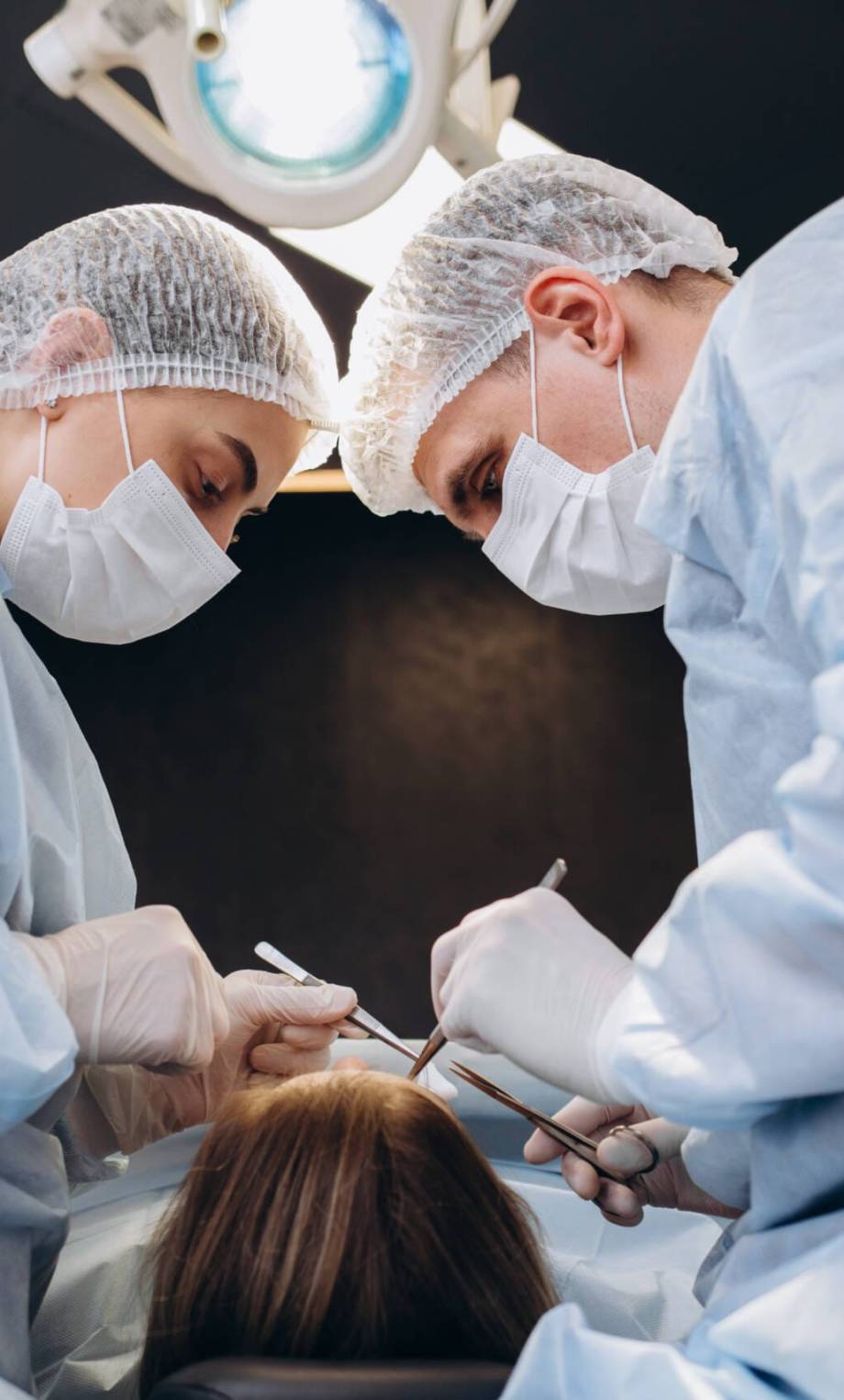 Professional medical team performing surgical operation in modern operating room. Asian assistant hands out instruments to surgeons doctor during operation on intensive care patient in hospital.